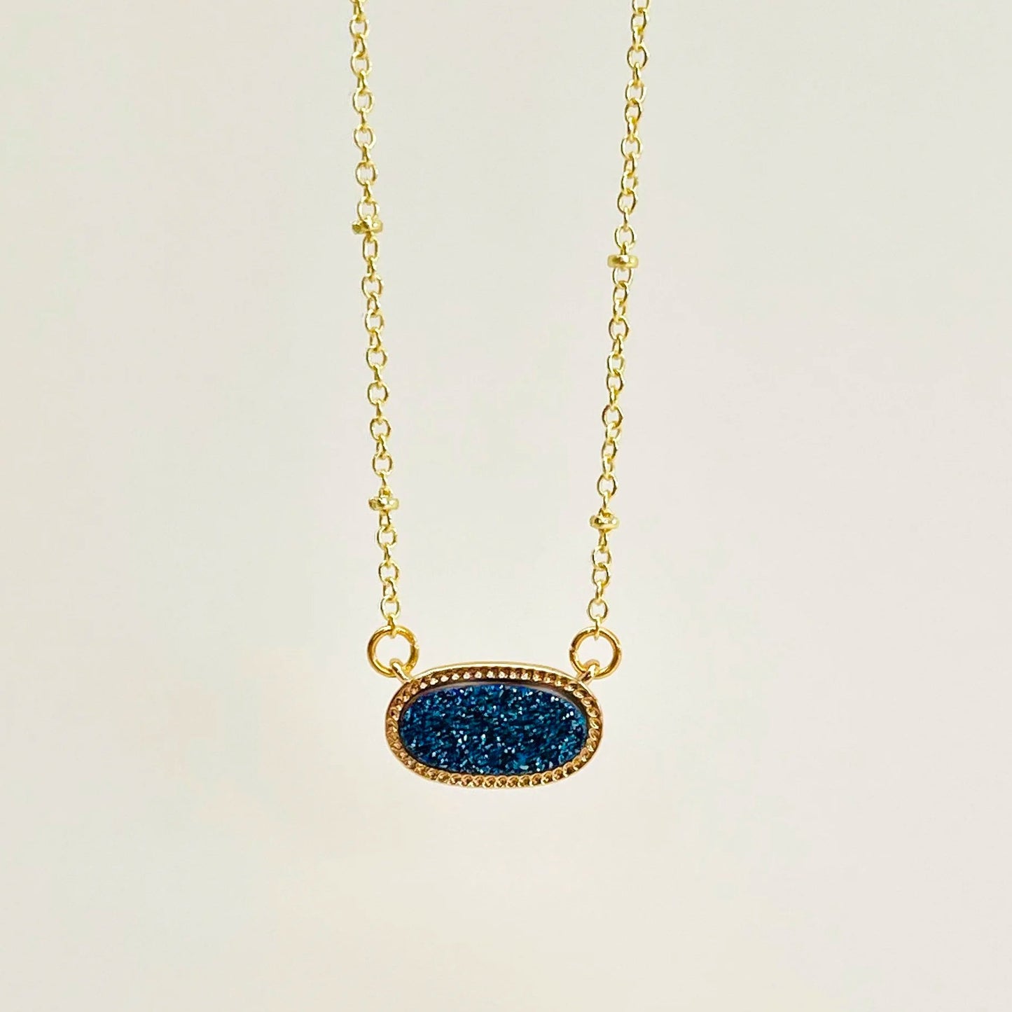 Blue Druzy Oval Pendant Gold Necklace on a light beige background