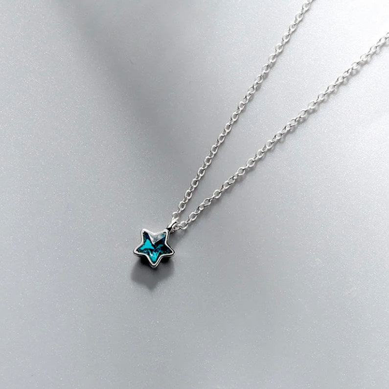 Star-shaped pendant necklace with blue gem on a light gray background