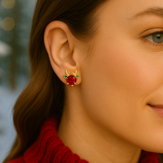 Close-up of a woman wearing a Holiday Red & Green Reindeer Earring with a red gemstone against a blurred background.