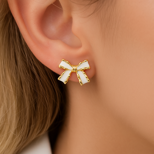 White and Gold Bow Earrings on a person's ear with a blurred background