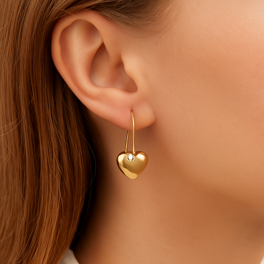 Gold heart drop earring worn by a woman with brown hair.