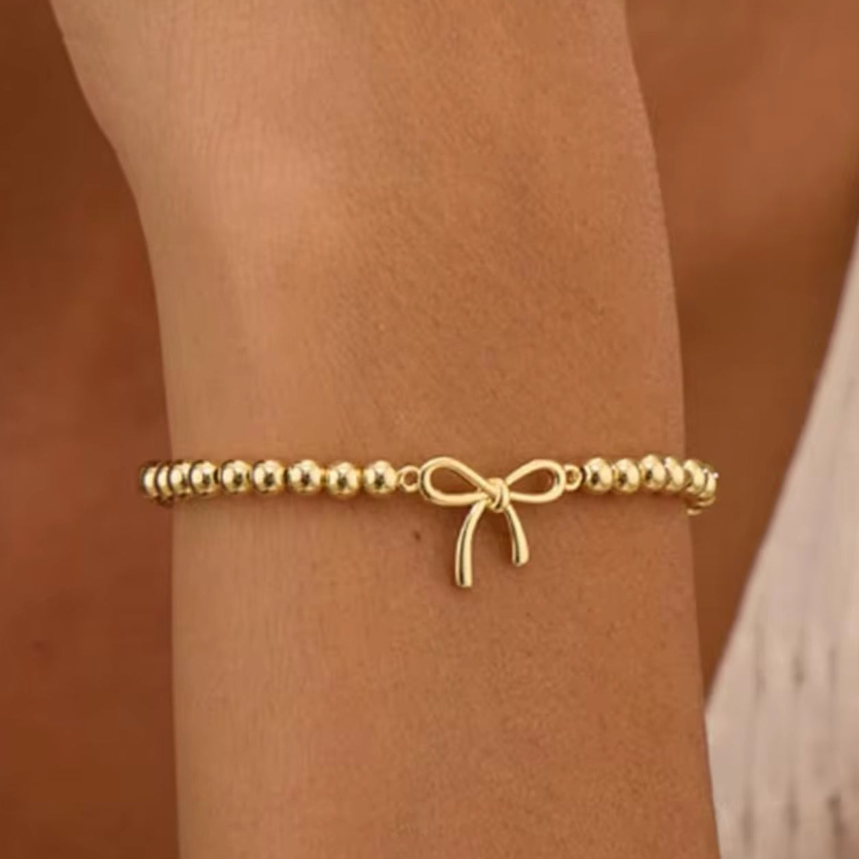 Gold Bow Bead Bracelet, on a wrist against a brown background