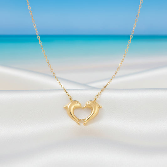 Gold heart necklace with a heart and dolphin design against a beach background