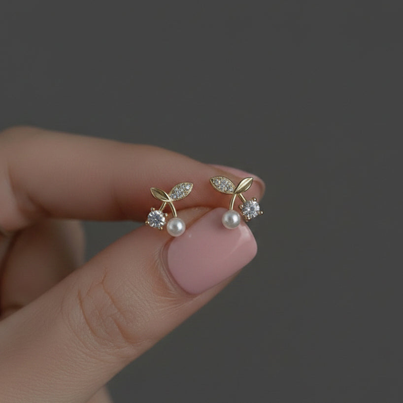 Gold earrings with pearls and gemstones held between fingers against a dark background