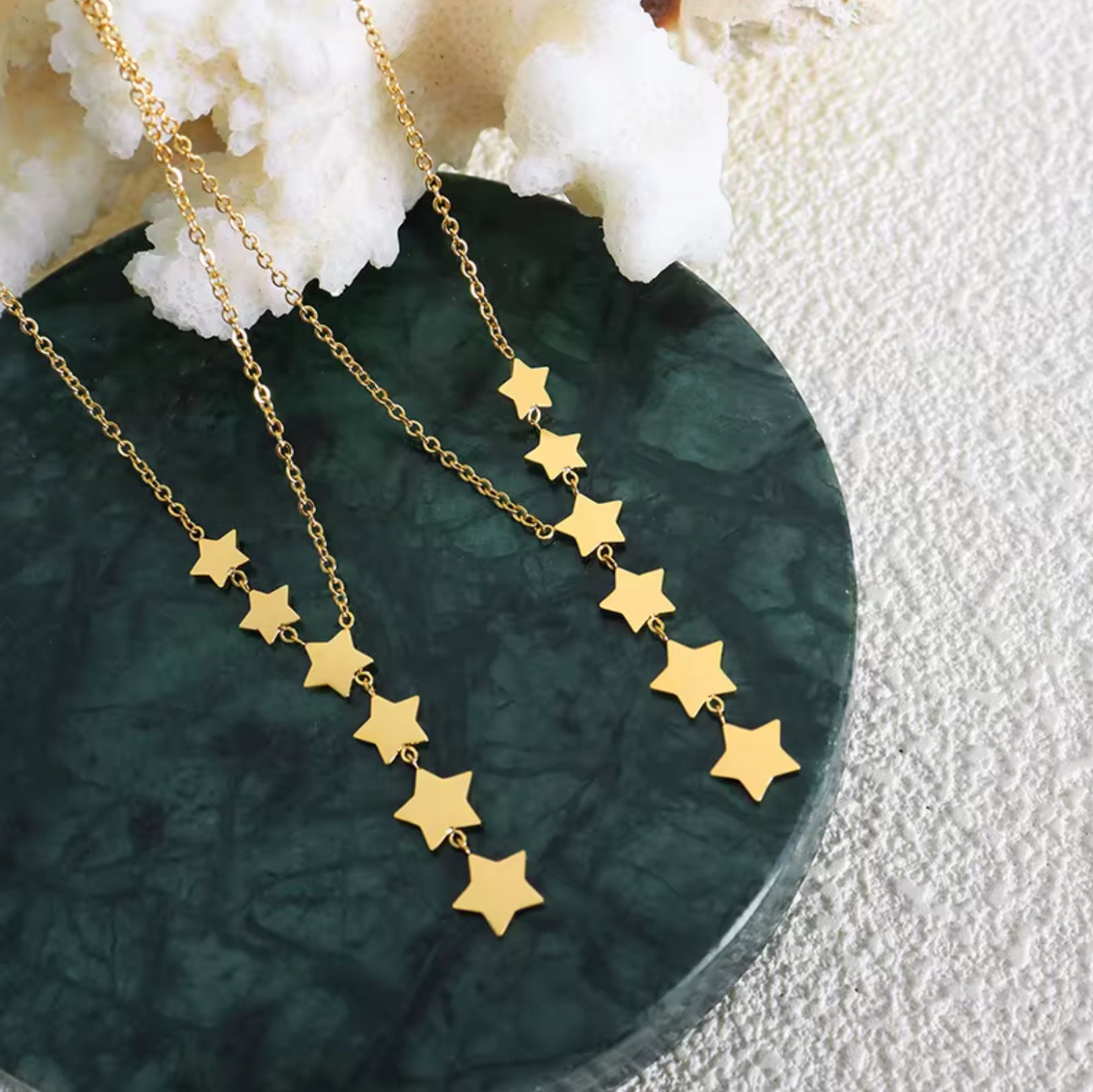 Gold star necklace on a green stone surface with white coral in the background