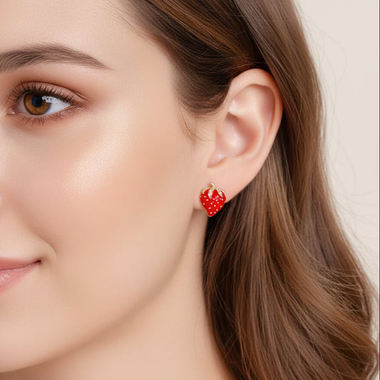 Red strawberry-shaped earrings being held near an ear on a neutral background