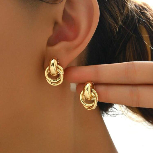 A close-up image of a woman's ear wearing a gold-tone circle knot earring.