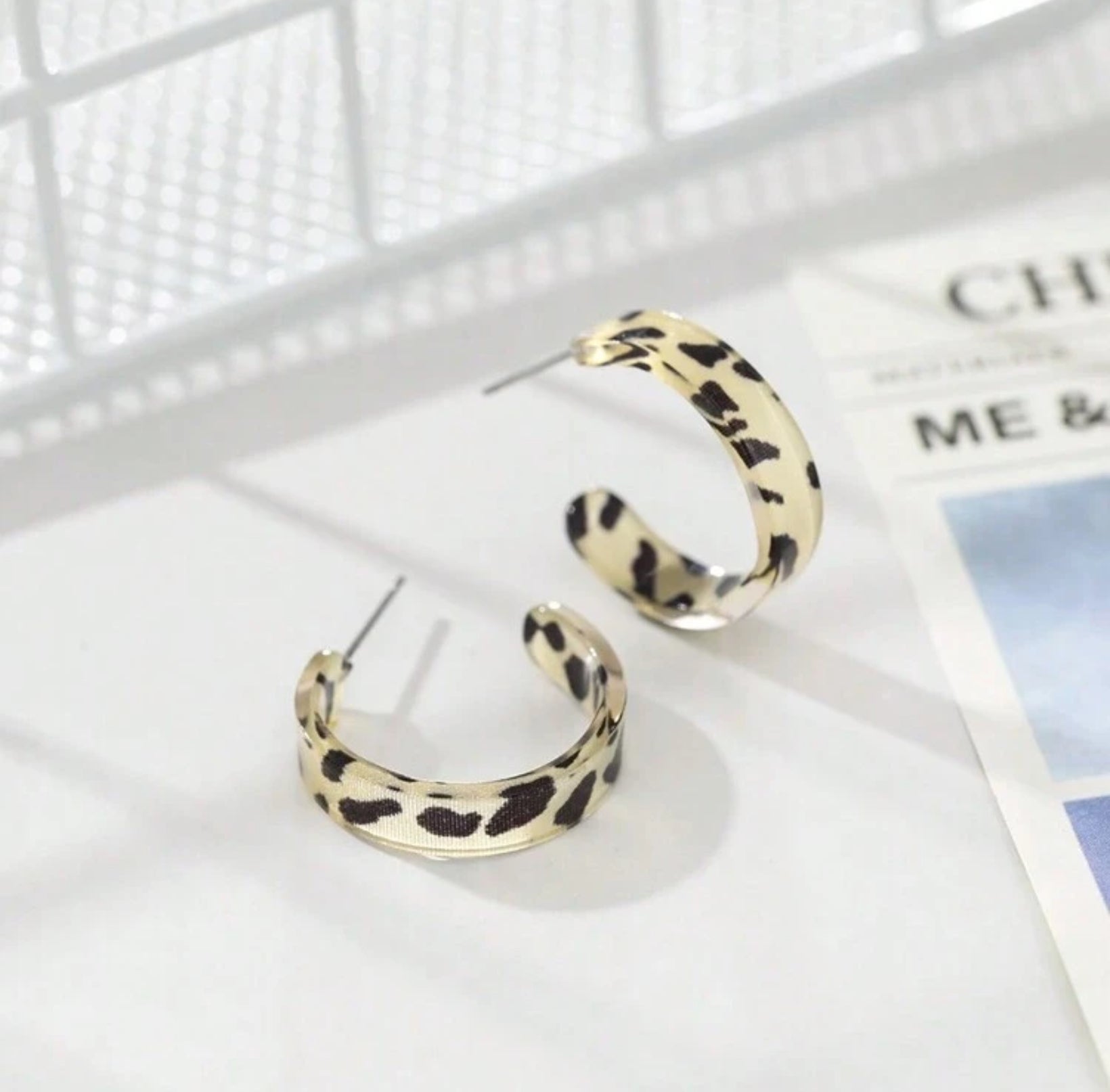 Leopard print hoop earrings on a white surface with a magazine in the background