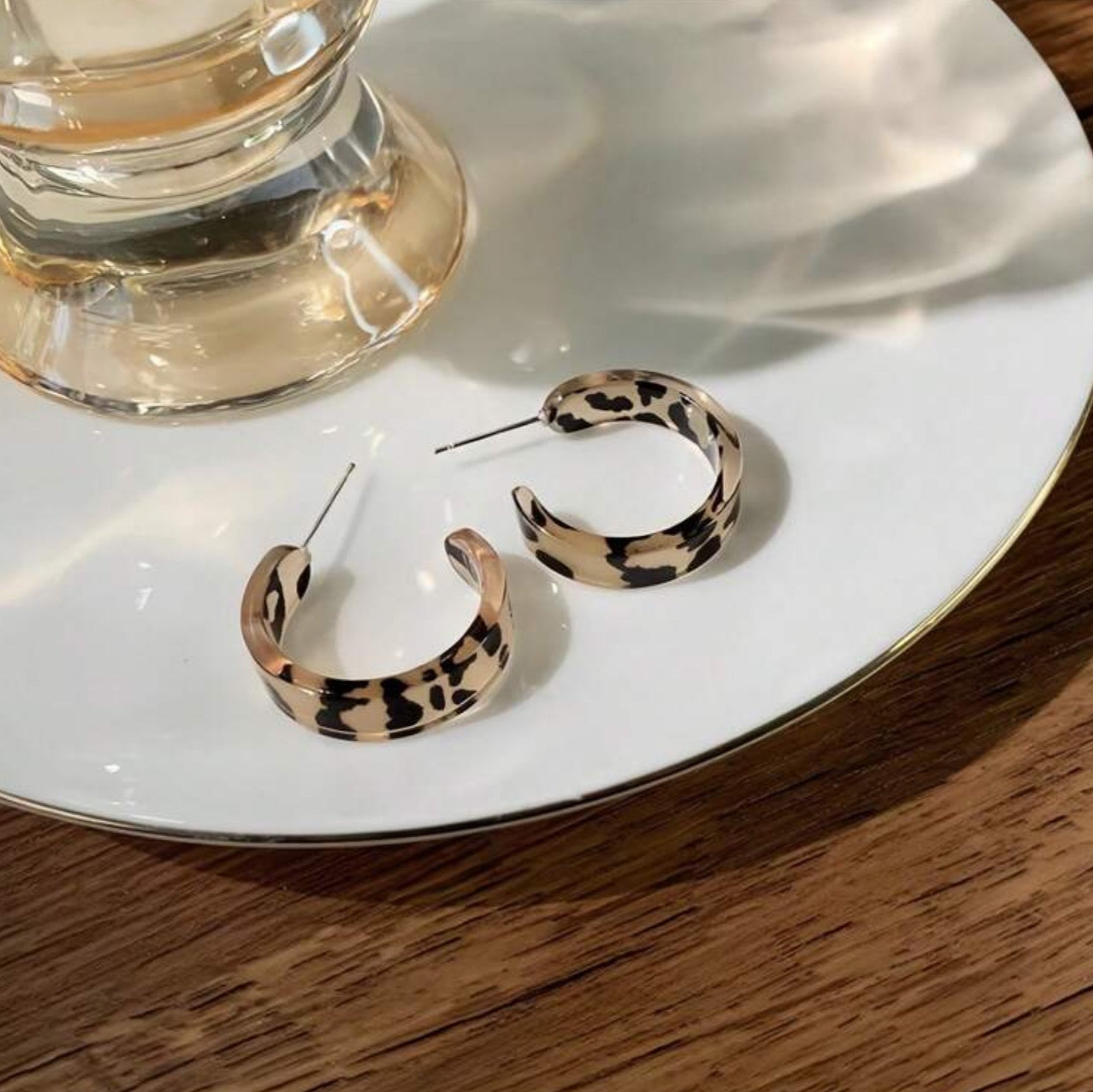Leopard print hoop earrings on a white plate with a glass of water.