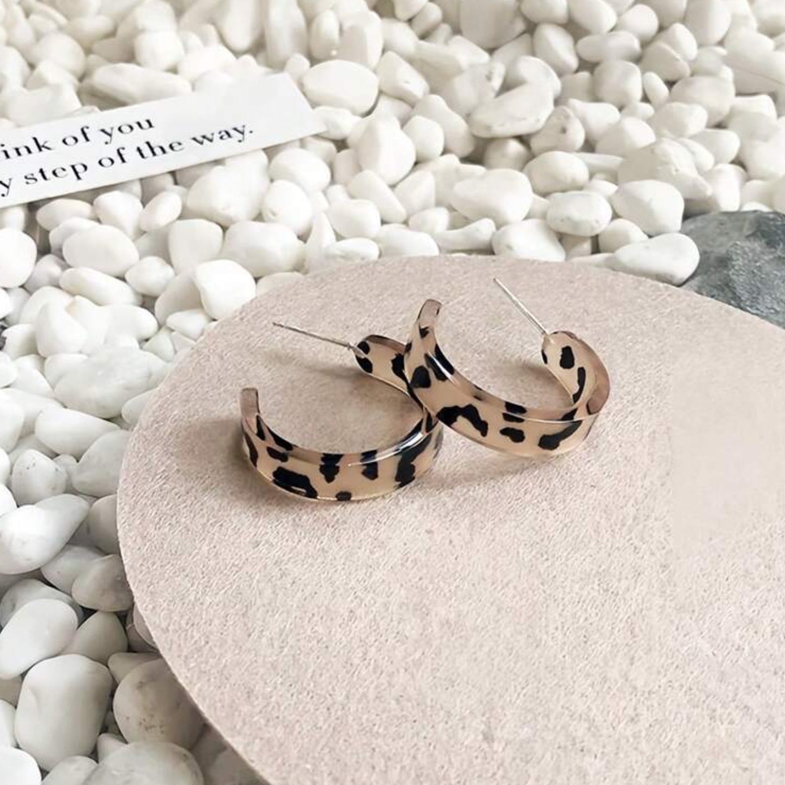 Leopard print hoop earrings on a stone surface with pebbles in the background