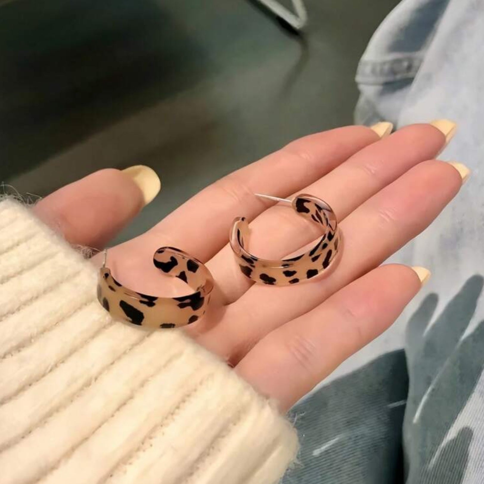 Leopard print hoop earrings held in a hand with a blurred background