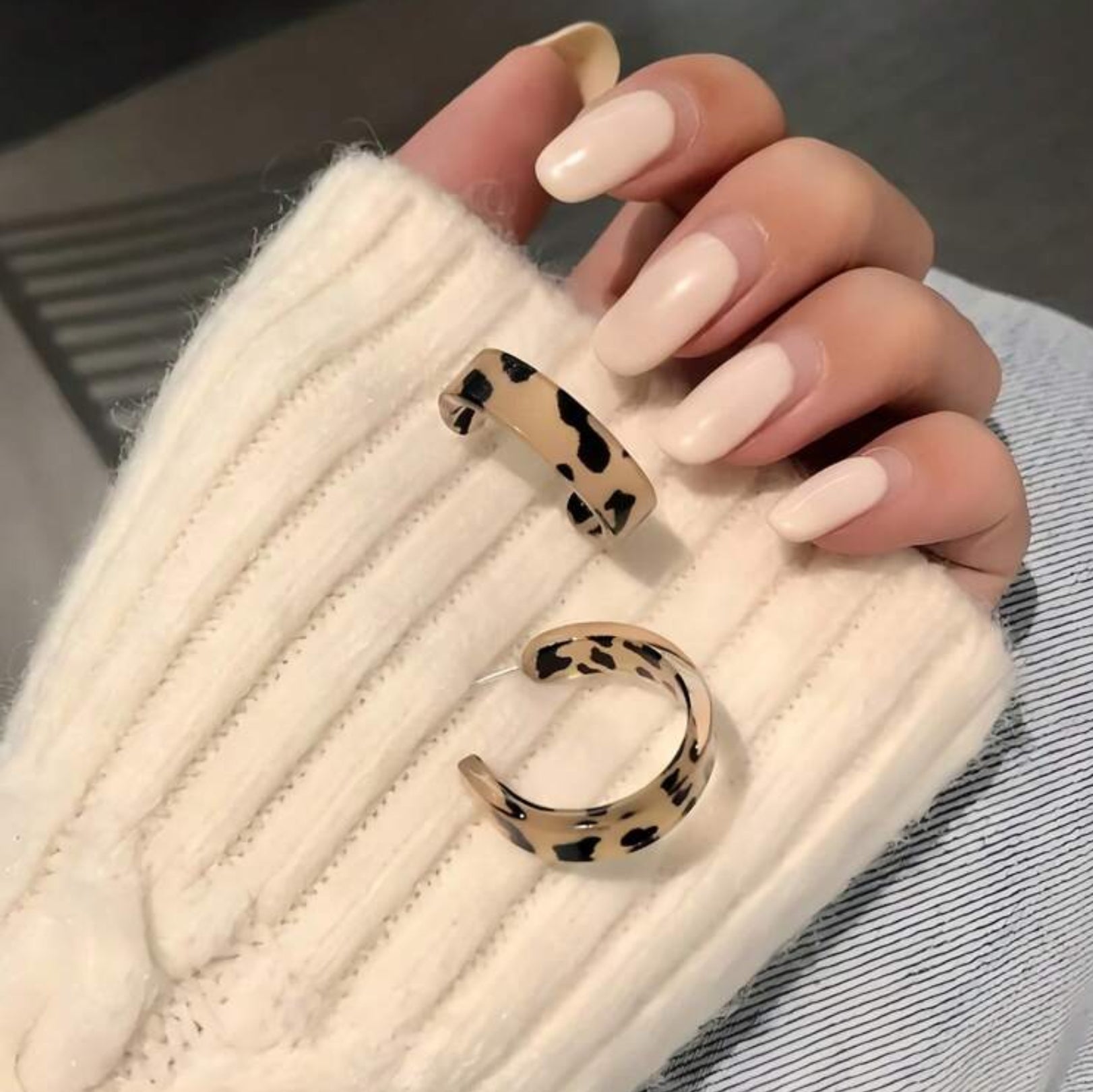 Leopard print hoop earrings held by a hand with light pink nail polish.