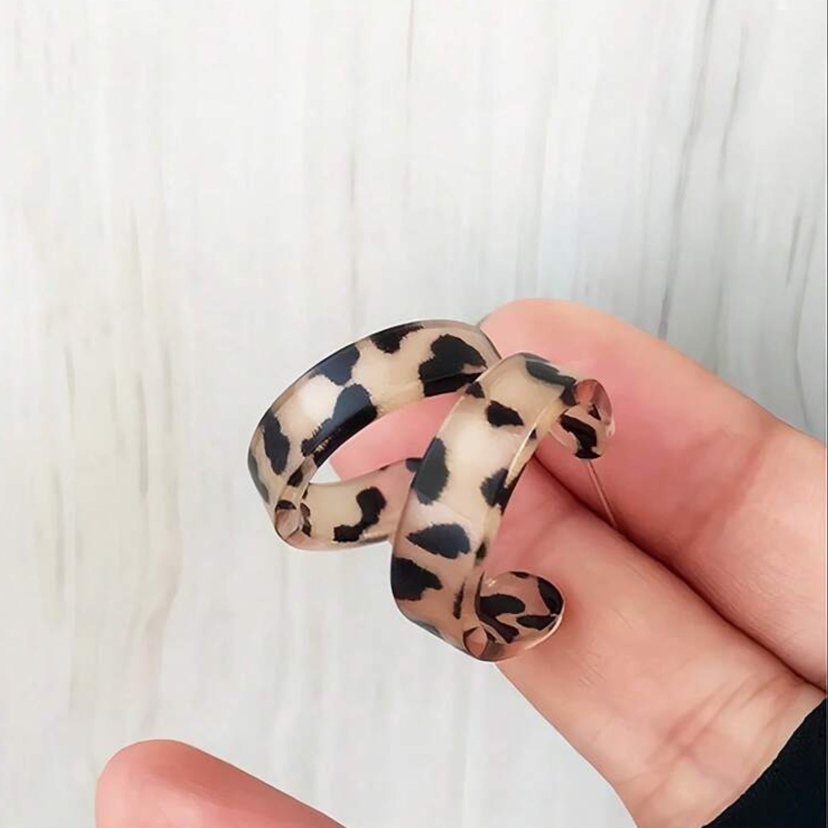 Leopard print hoop earrings held by a hand against a white background