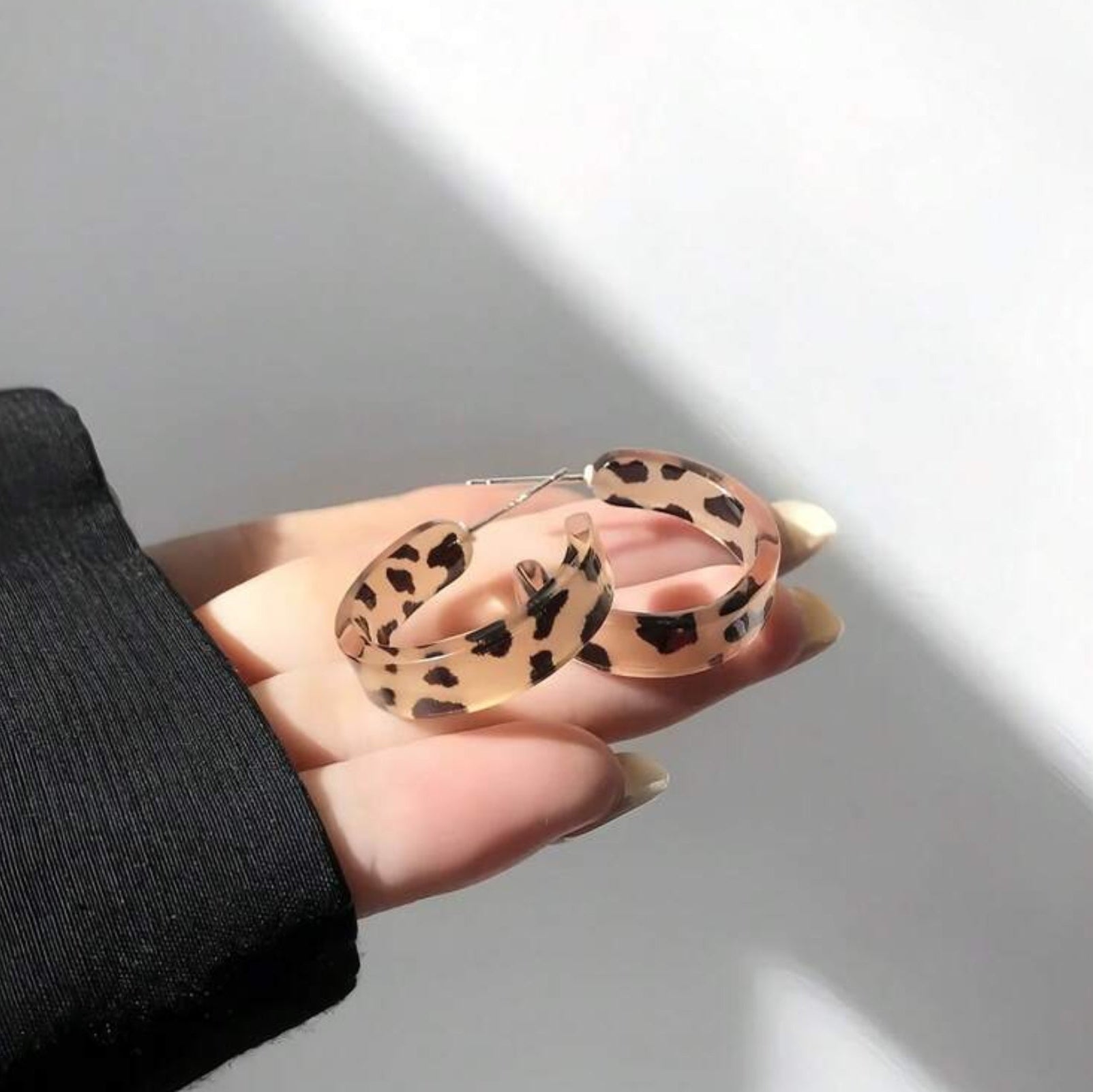 Hand holding leopard print hoop earrings against a neutral background