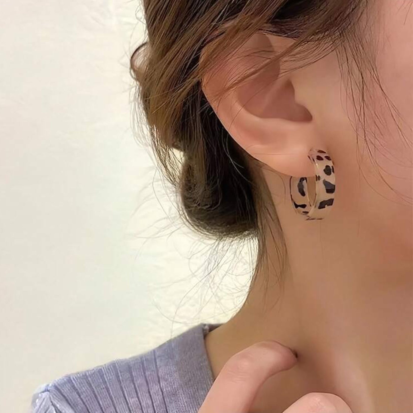 Leopard print hoop earring worn by a person with a neutral background