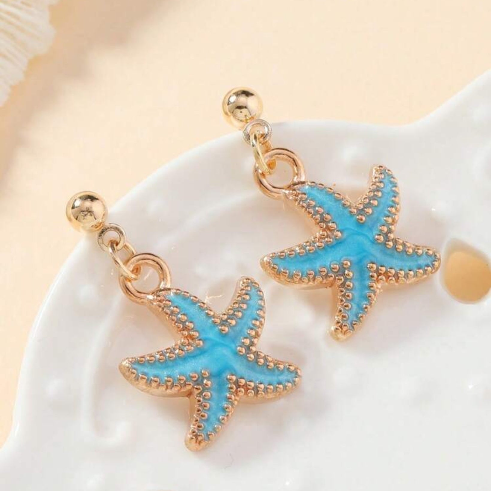 Starfish-shaped earrings with blue stones on a white stone background