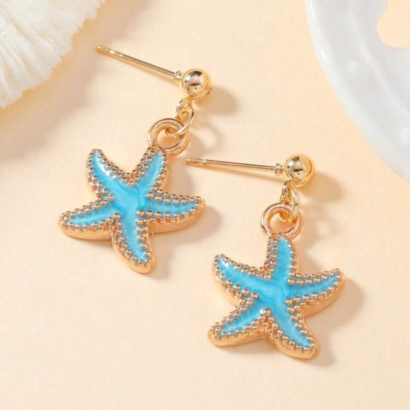 Starfish-shaped earrings with blue centers and gold outlines on a beige background