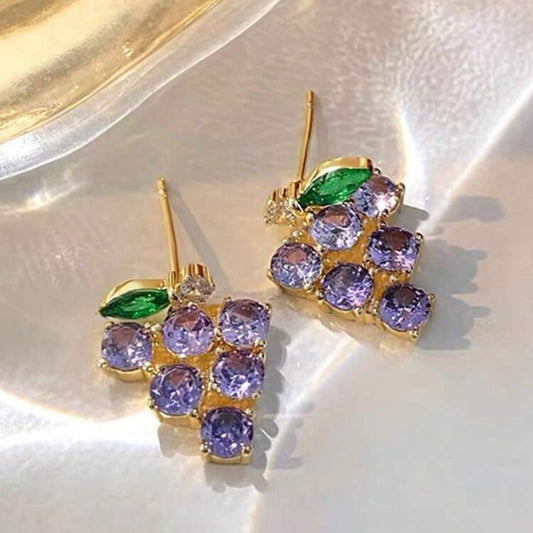 Gold earrings with purple gemstones and green leaves on a white background