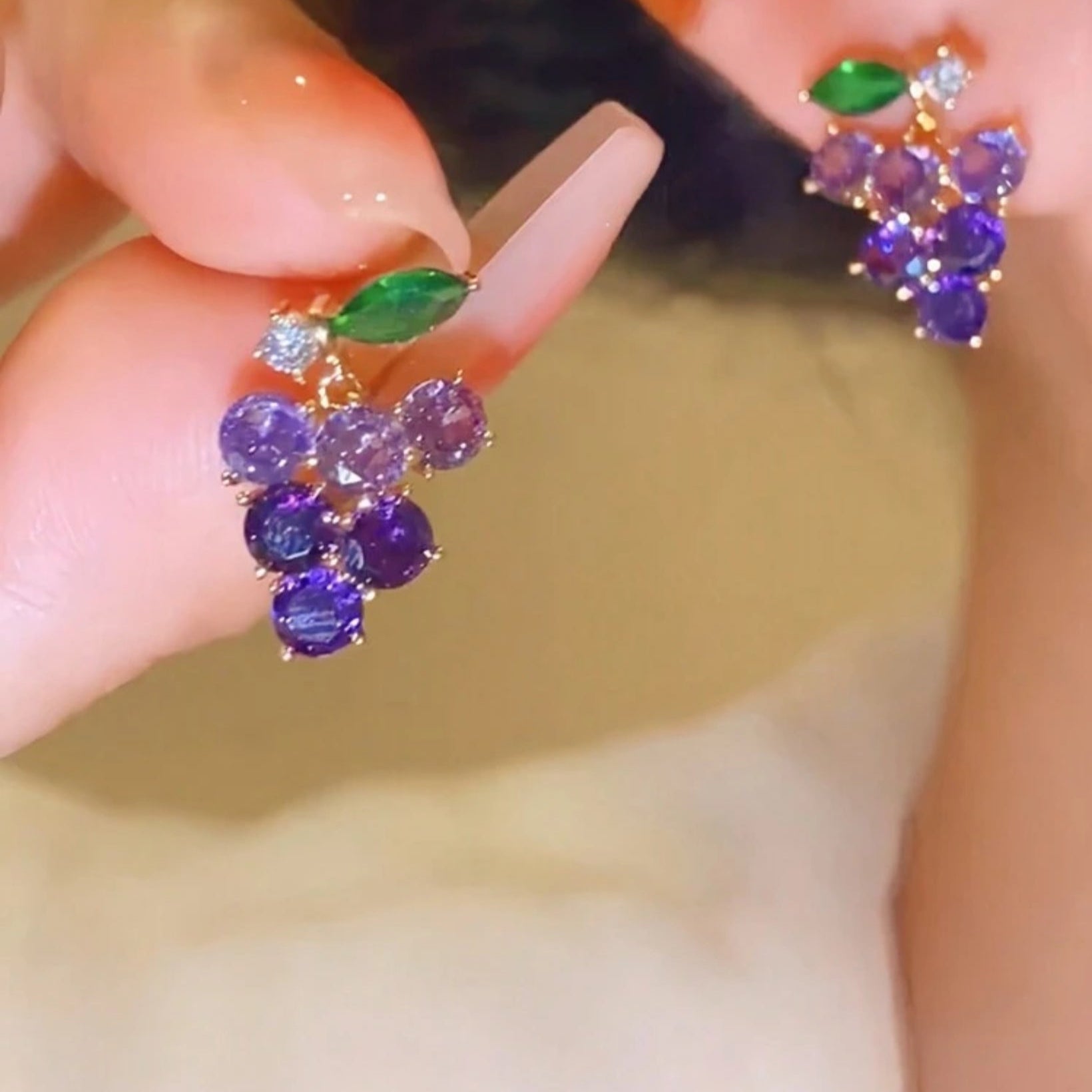 Close-up of a hand wearing purple gemstone earrings with green leaves on a blurred background