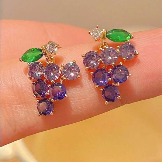 Grape-shaped earrings with purple and green stones on a hand