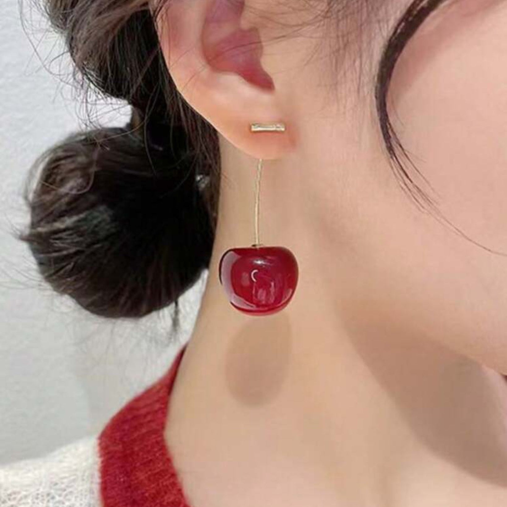Close-up of a cherry-shaped earring worn by a person with a blurred background