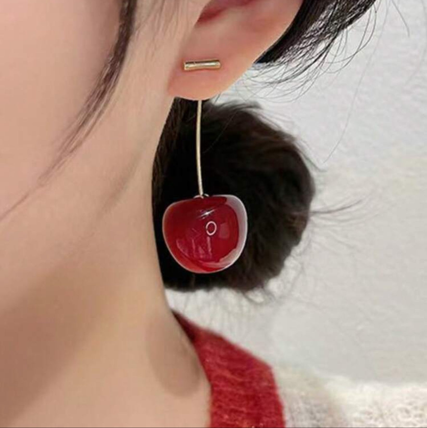 Close-up of an ear wearing a cherry-shaped earring with a white background