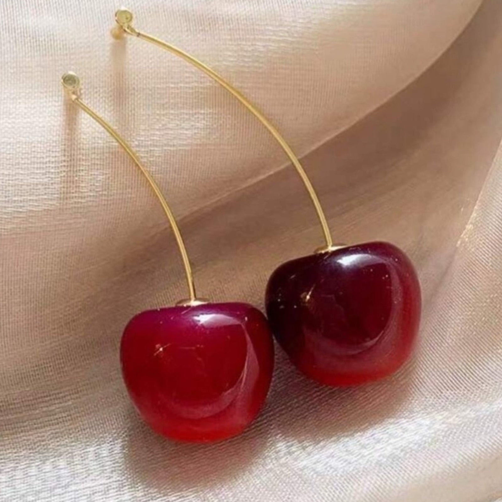 Cherry-shaped earrings on a beige fabric background
