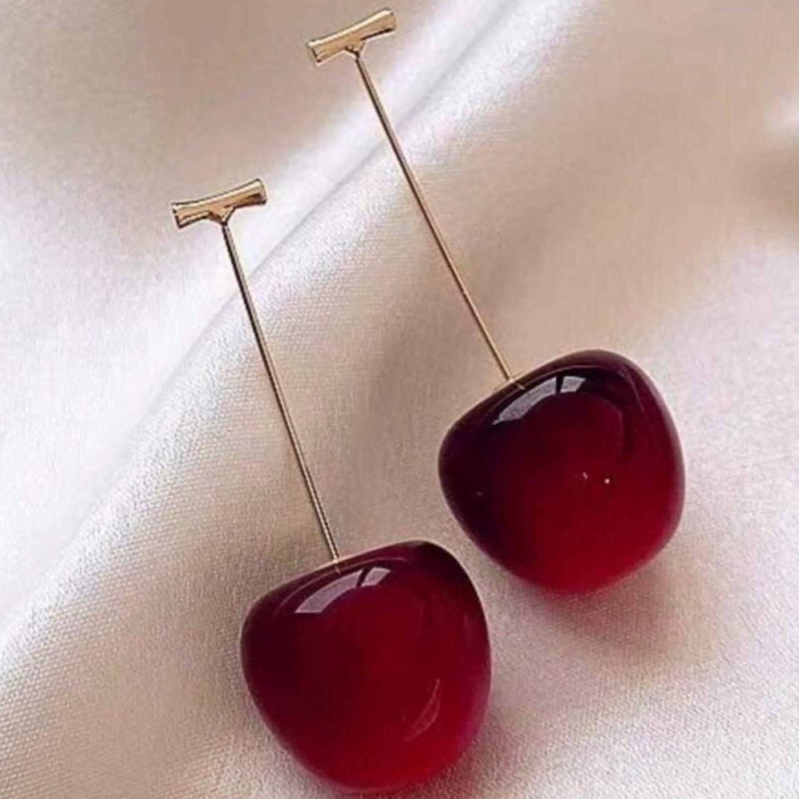 Cherry-shaped earrings with gold t-shaped stems on a light background