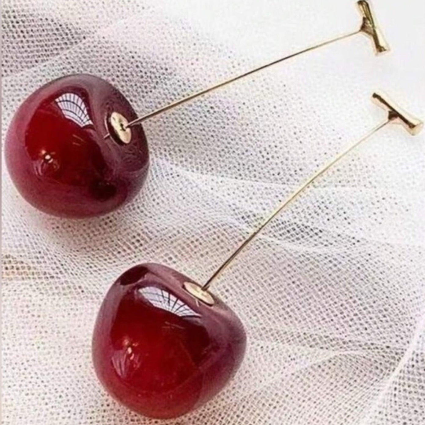 Cherry-shaped earrings on a textured white background
