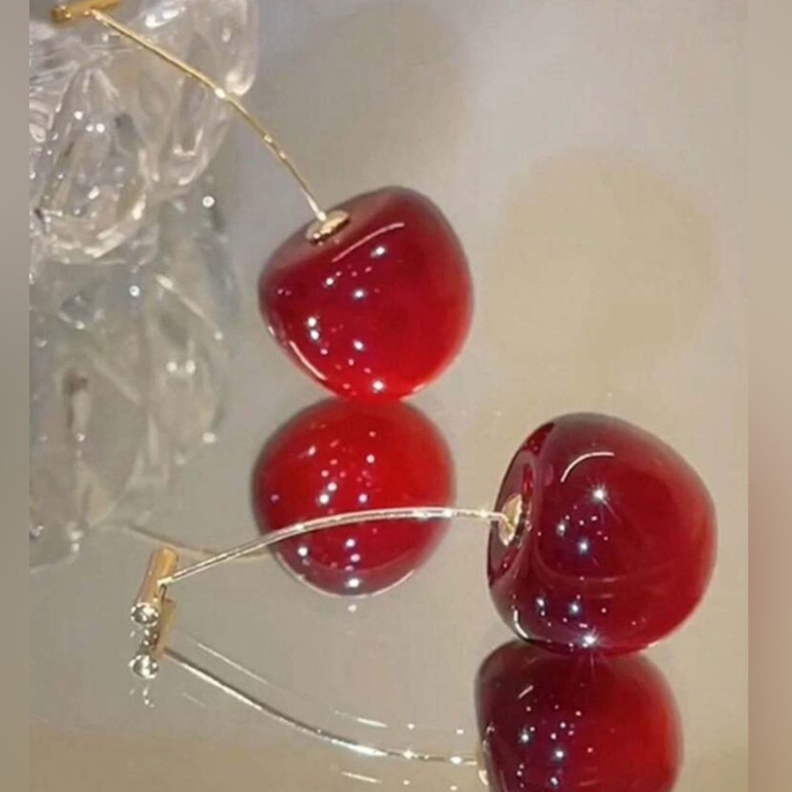 Red cherry earrings with gold hooks on a reflective surface