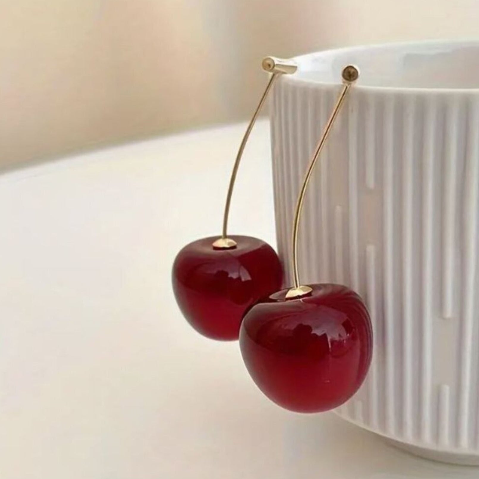Cherry-shaped earrings on a white surface with a blurred background