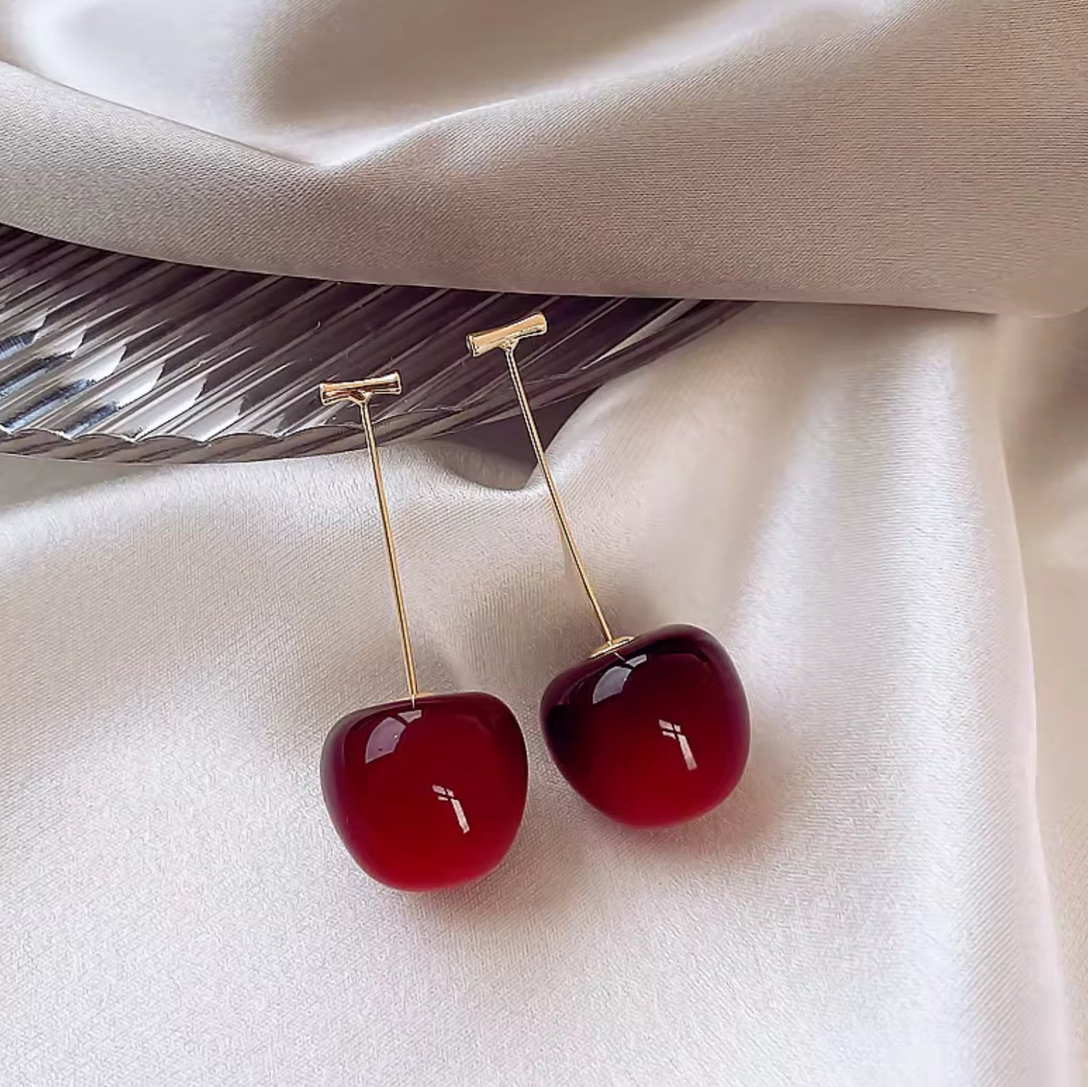 Cherry-shaped earrings on a white fabric background