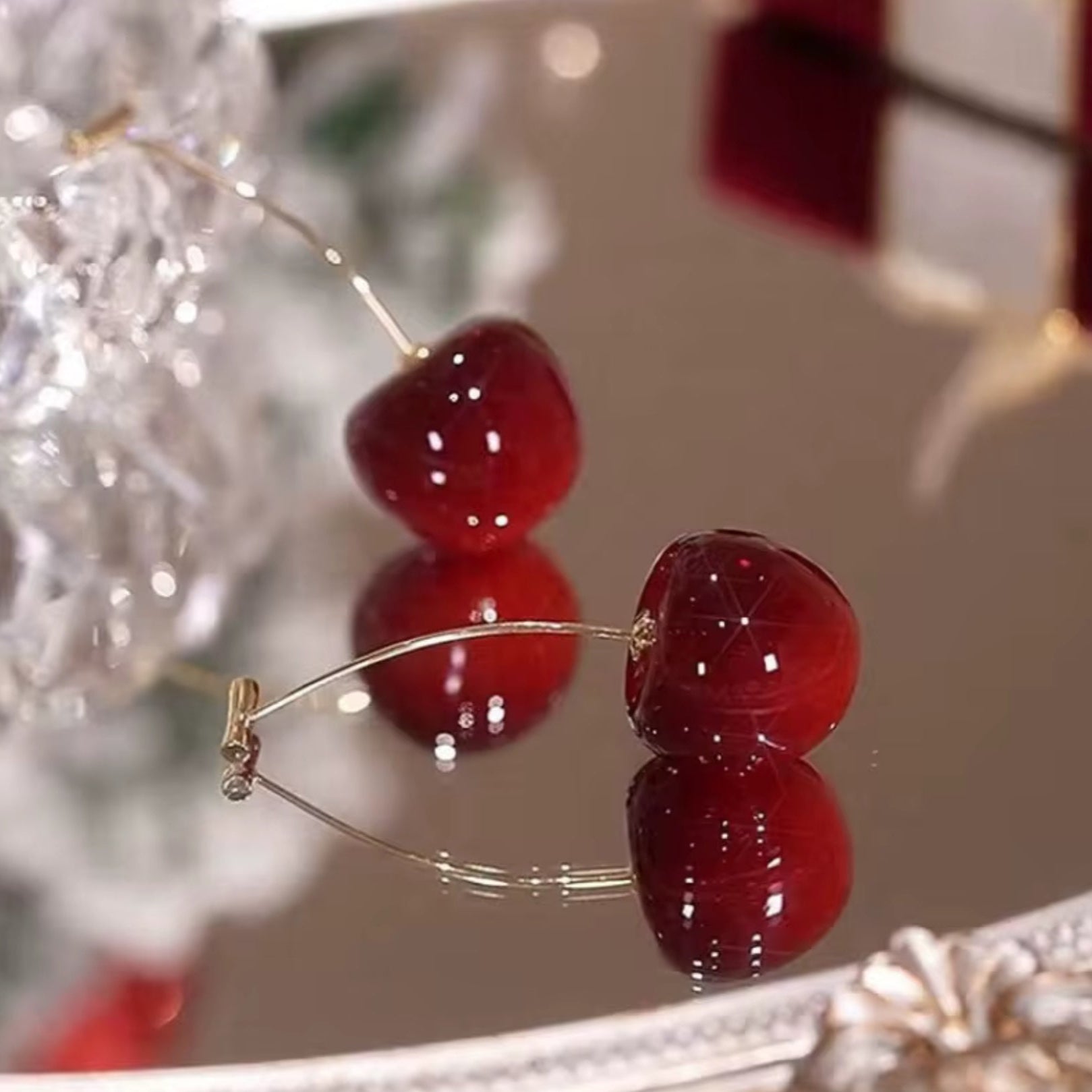 Cherry-themed earrings with red gemstones on a reflective surface.
