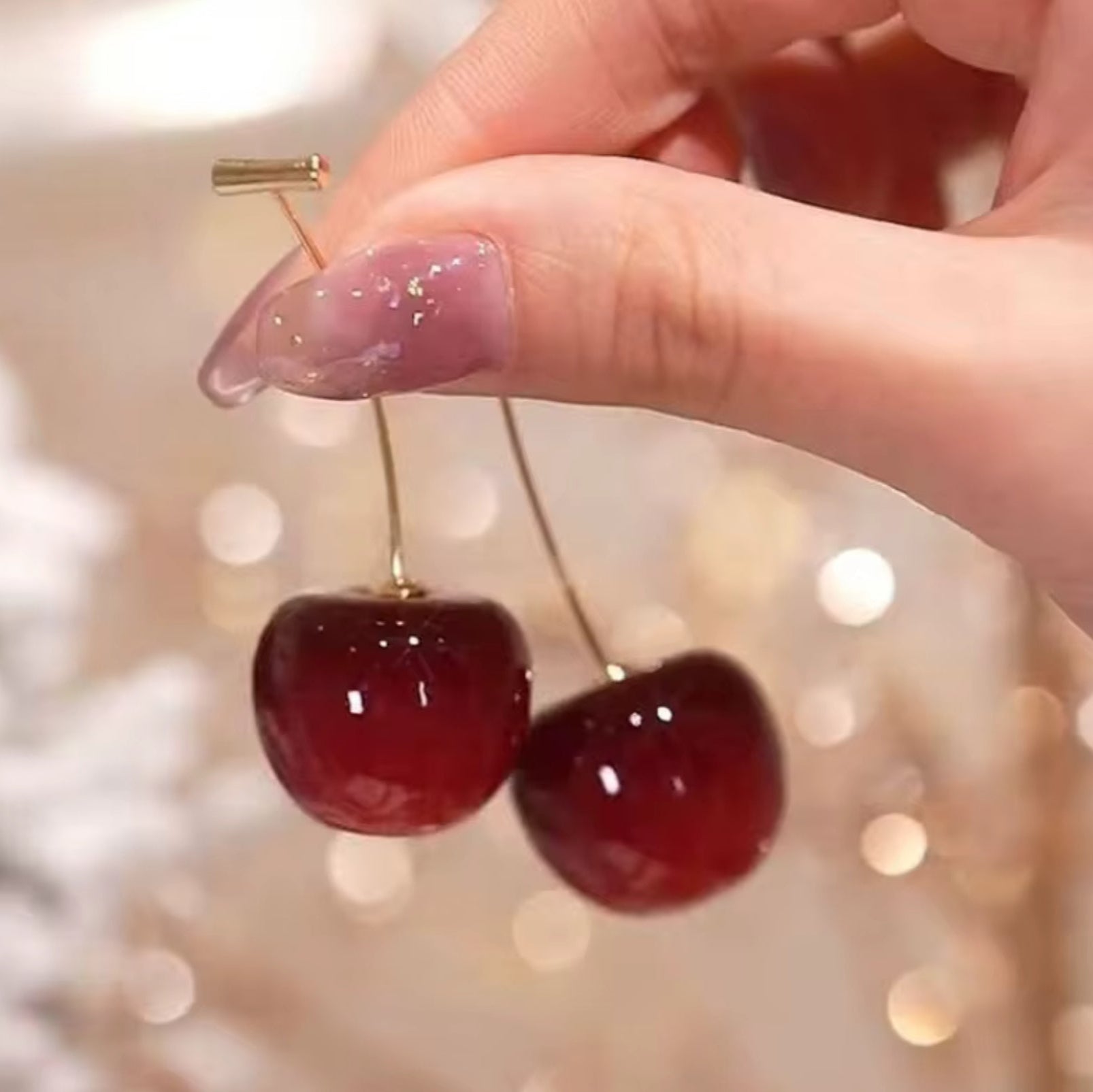 Cherry-shaped earrings held by a hand with a blurred light background