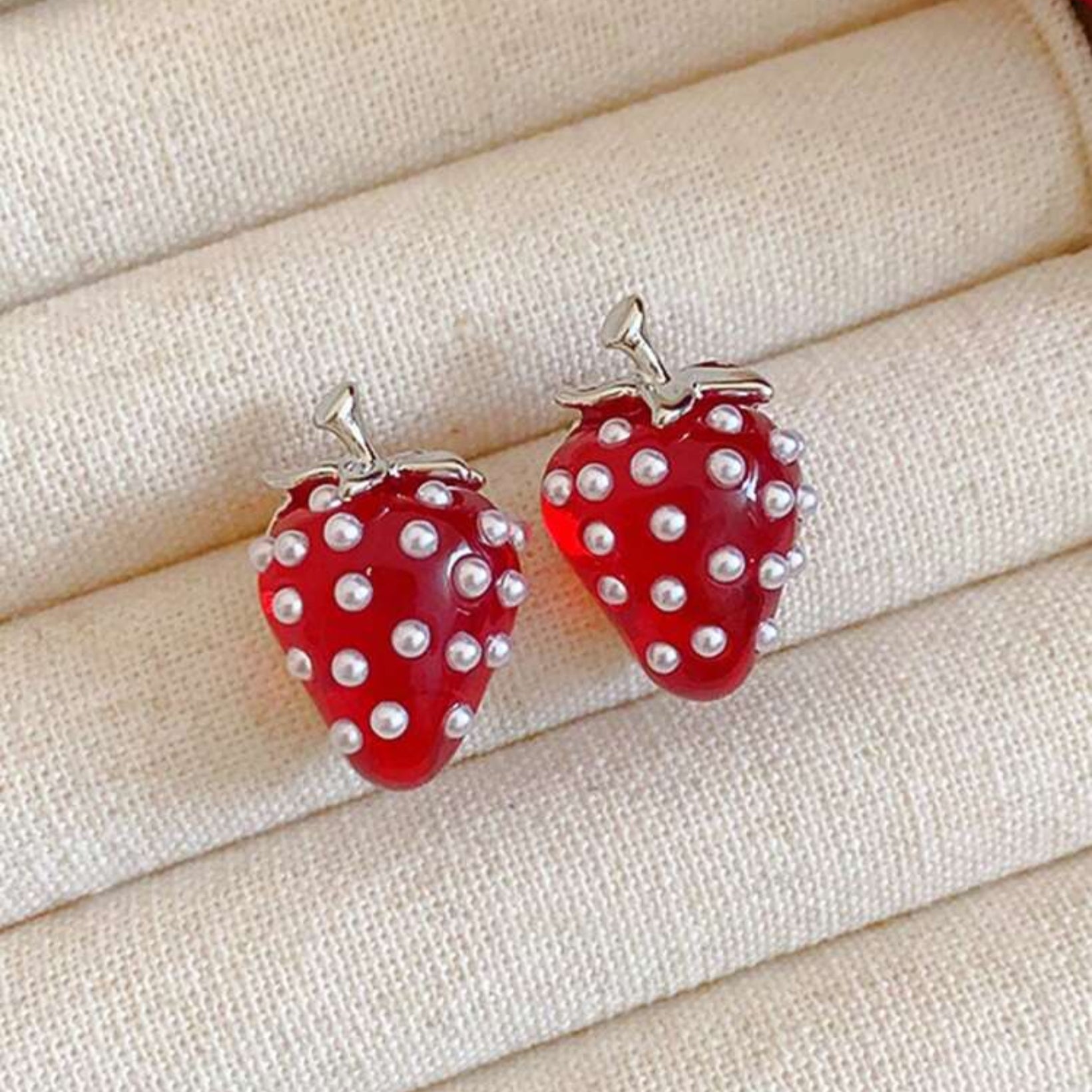 Red strawberry-shaped earrings with pearl-like embellishments on a beige fabric background
