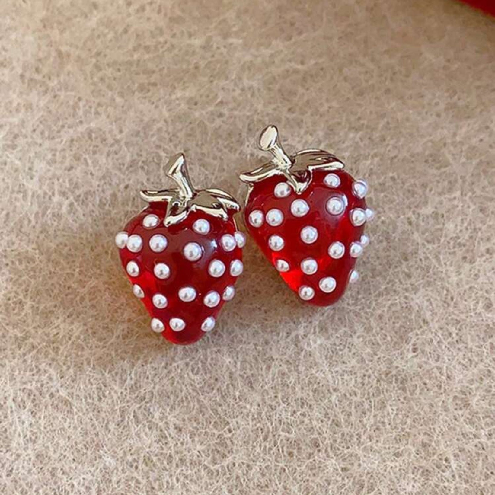 Red strawberry-shaped earrings with white polka dots on a beige background