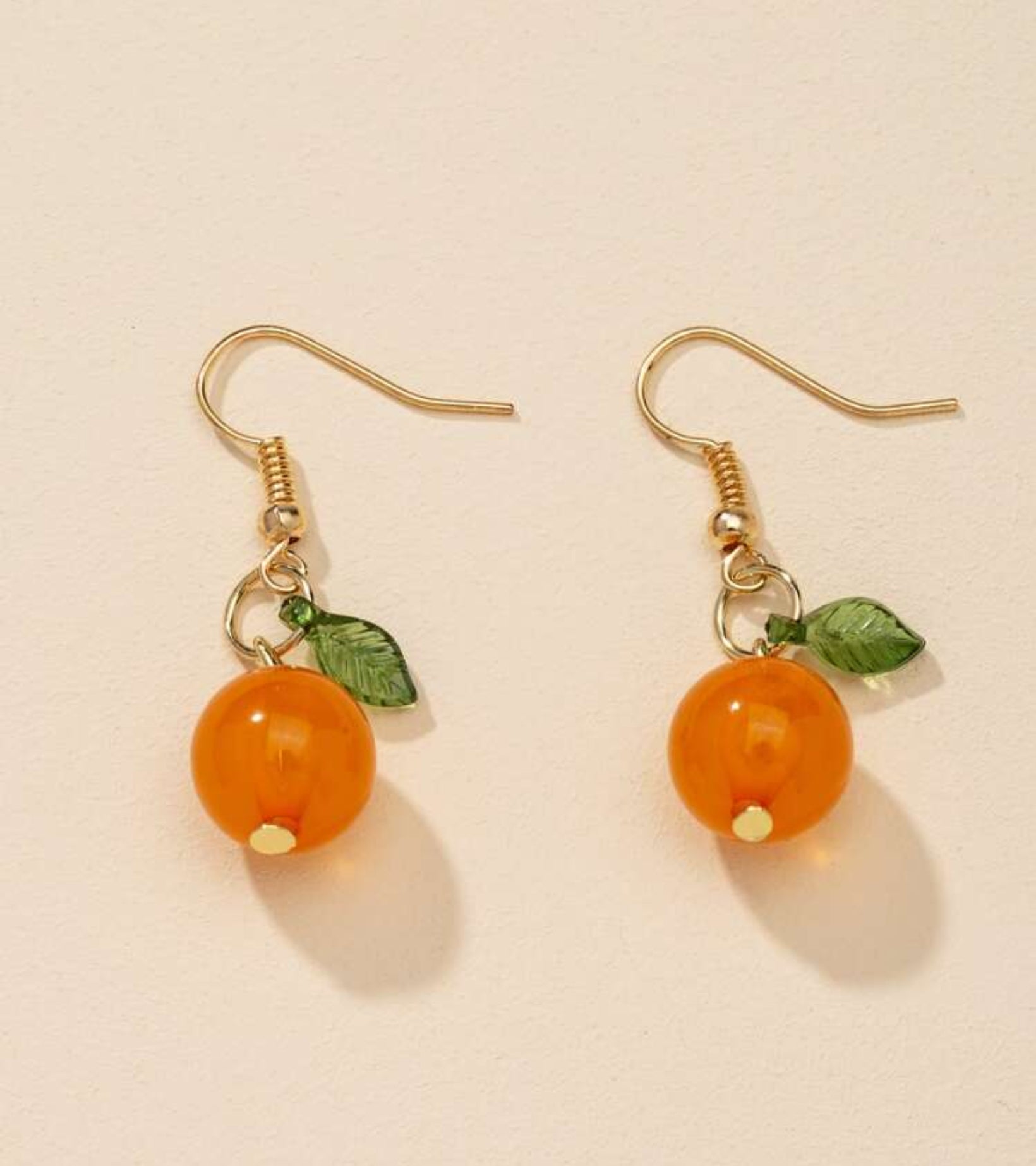 Pair of earrings with orange beads and green leaves on a beige background