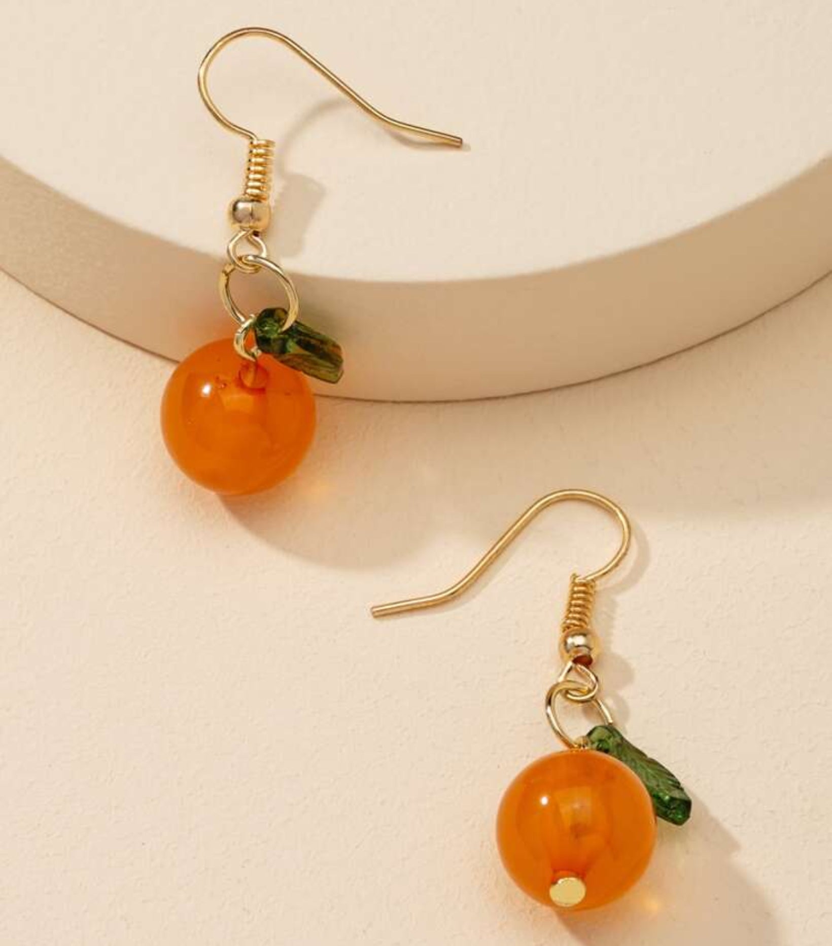 Orange fruit-shaped earrings with gold hooks on a beige background
