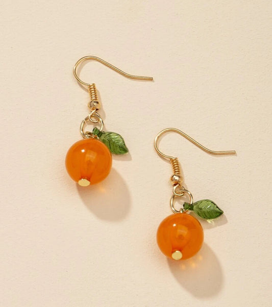 Pair of orange bead earrings with gold hooks and green leaves on a beige background