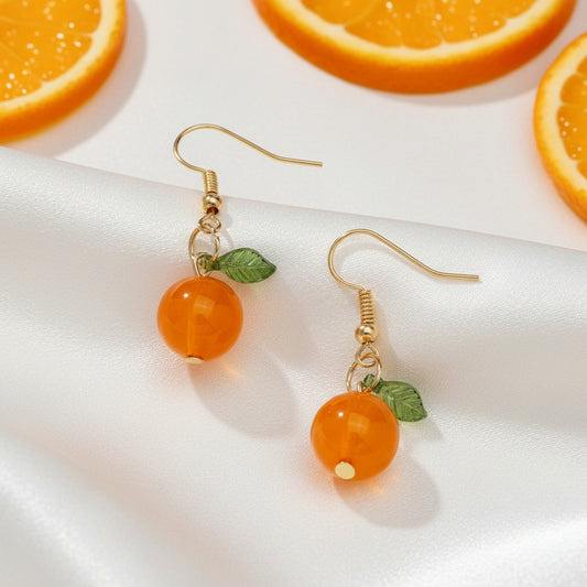 Pair of orange bead earrings with gold hooks and green leaves on a beige background