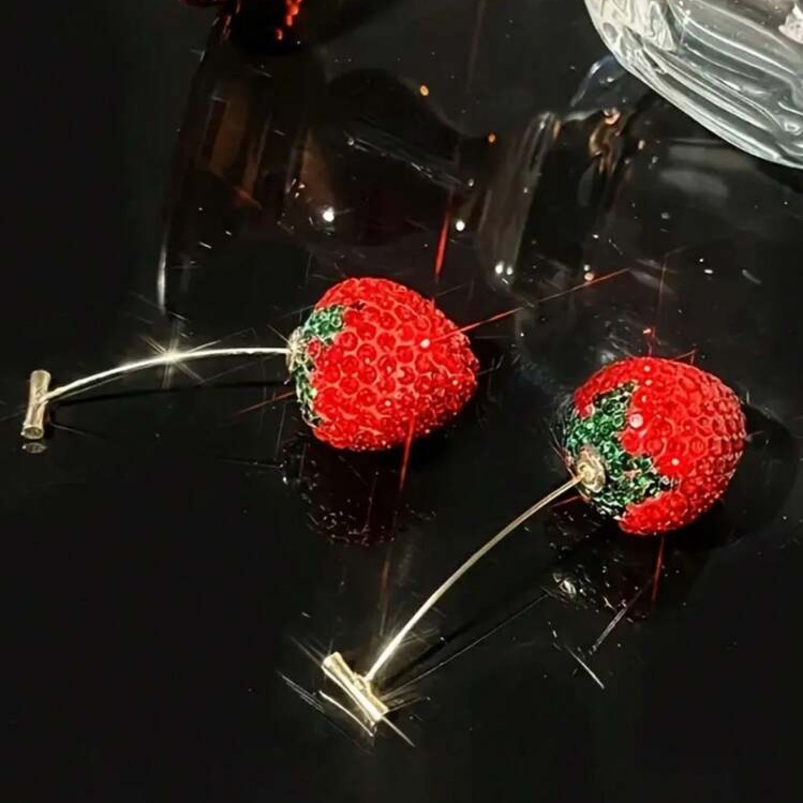 Strawberry-shaped earrings on a reflective black surface