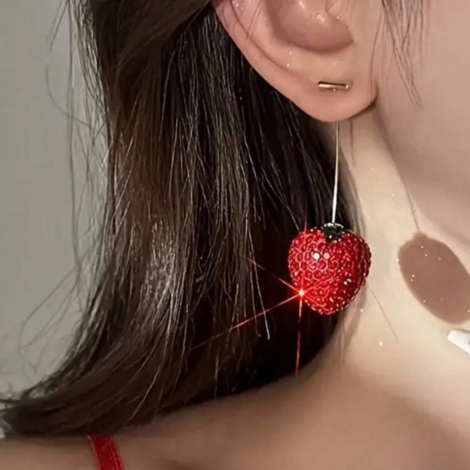Close-up of a person wearing a red heart-shaped earring with a sparkly effect.