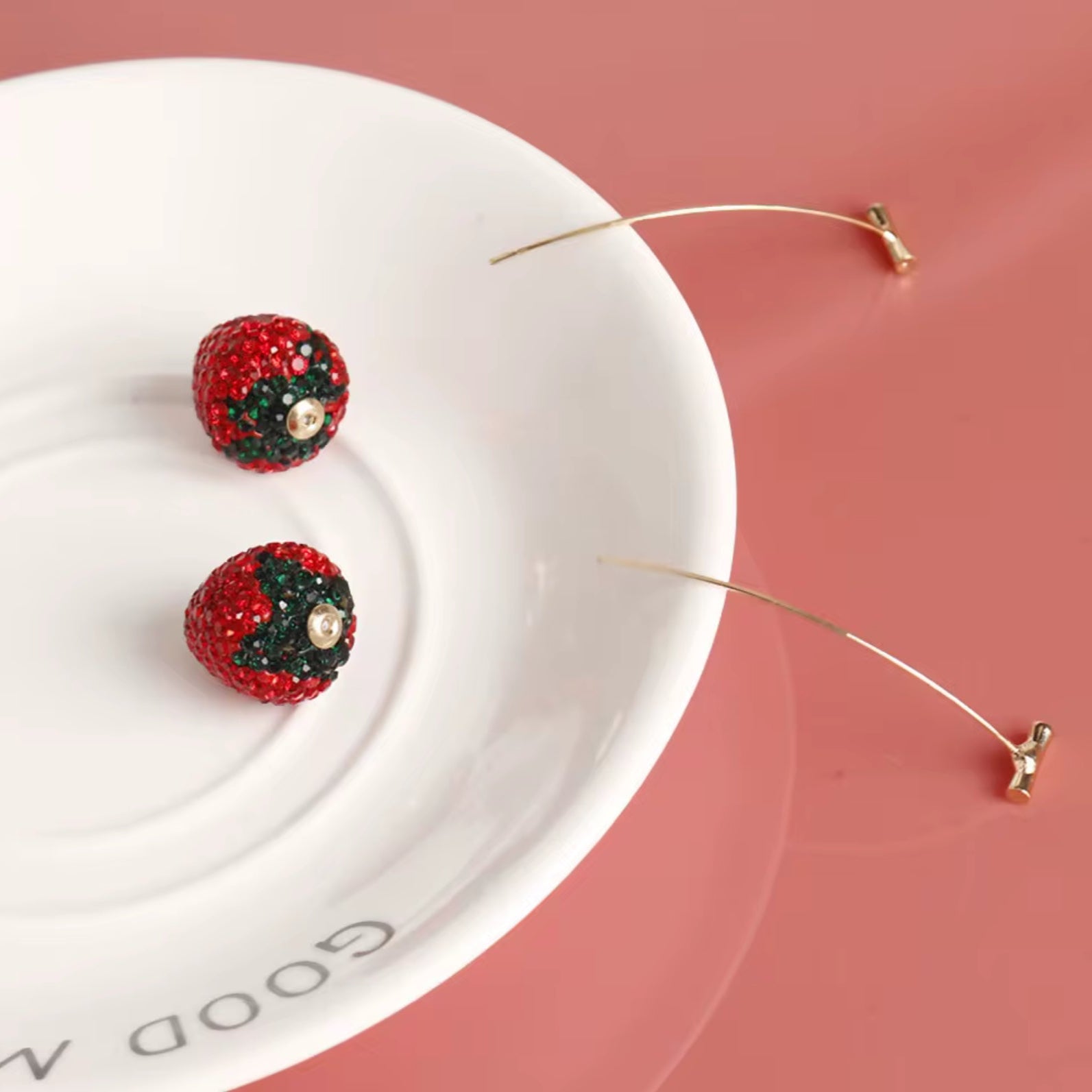 Red and black embellished earrings on a white dish with a pink background
