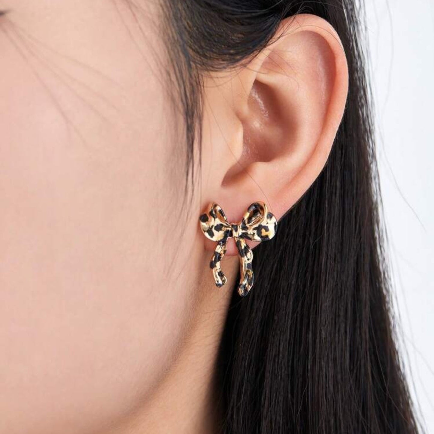 Leopard print bow-shaped earring worn by a person with dark hair.