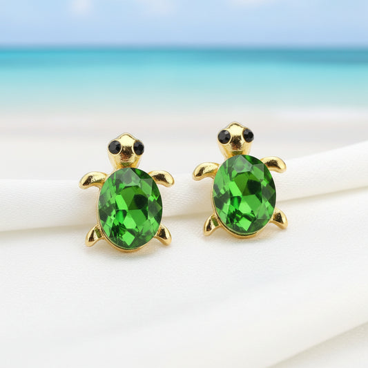 Green Gem Turtle Earrings with green gemstones on a blurred beach background