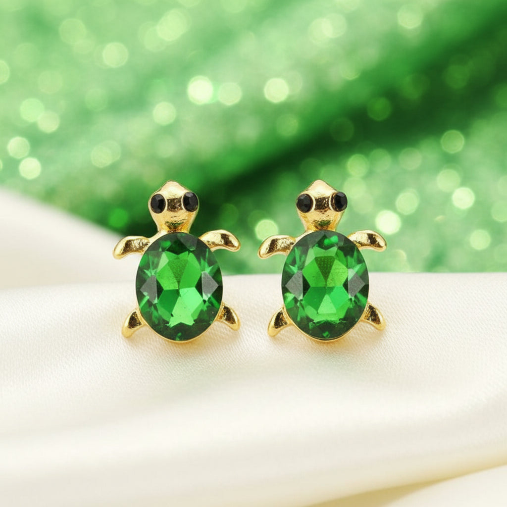 Green Gem Turtle Earrings with green gemstones on a white surface with a green glittery background