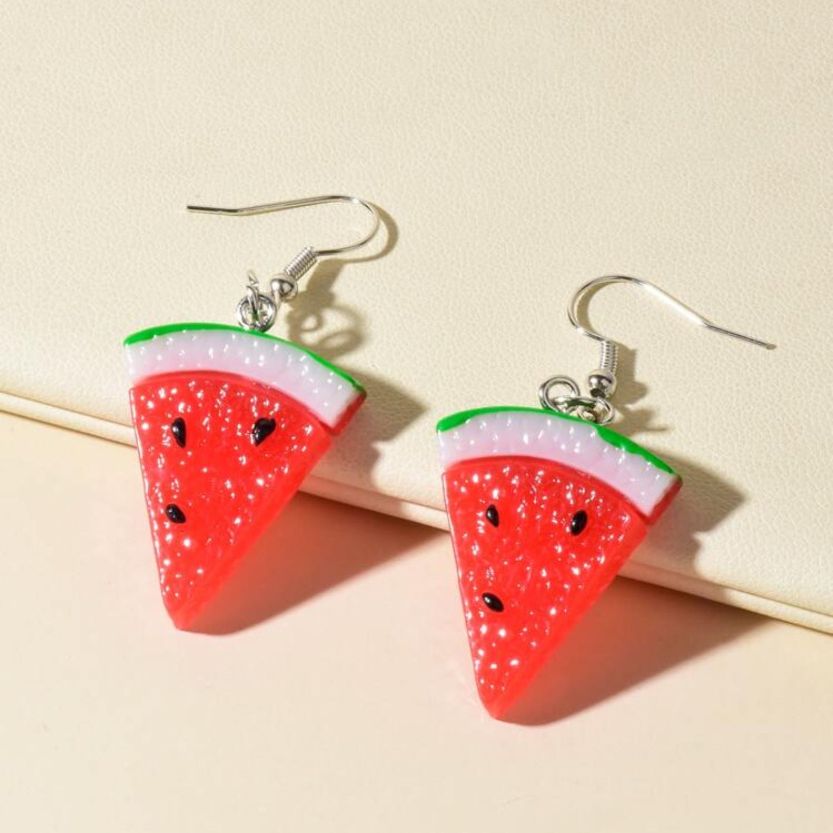 Watermelon slice earrings on a beige background