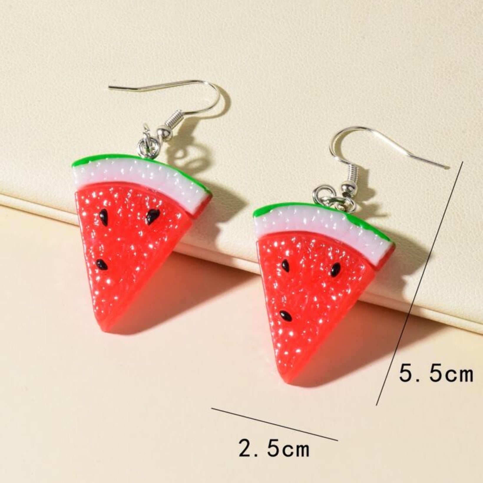 Watermelon slice earrings with measurements on a beige background
