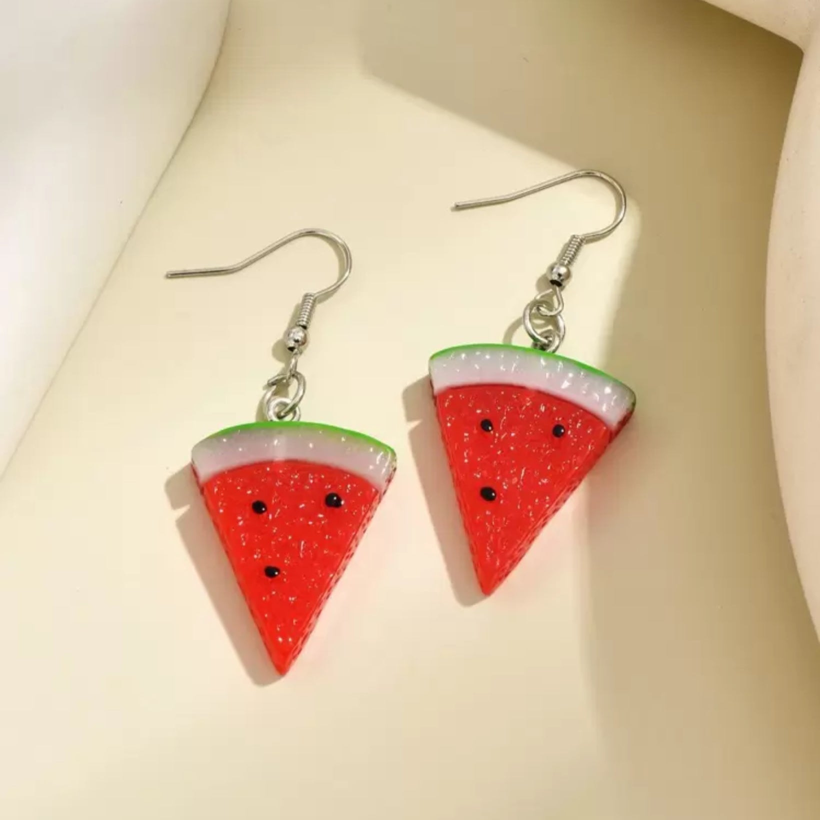 Watermelon slice earrings on a light beige background