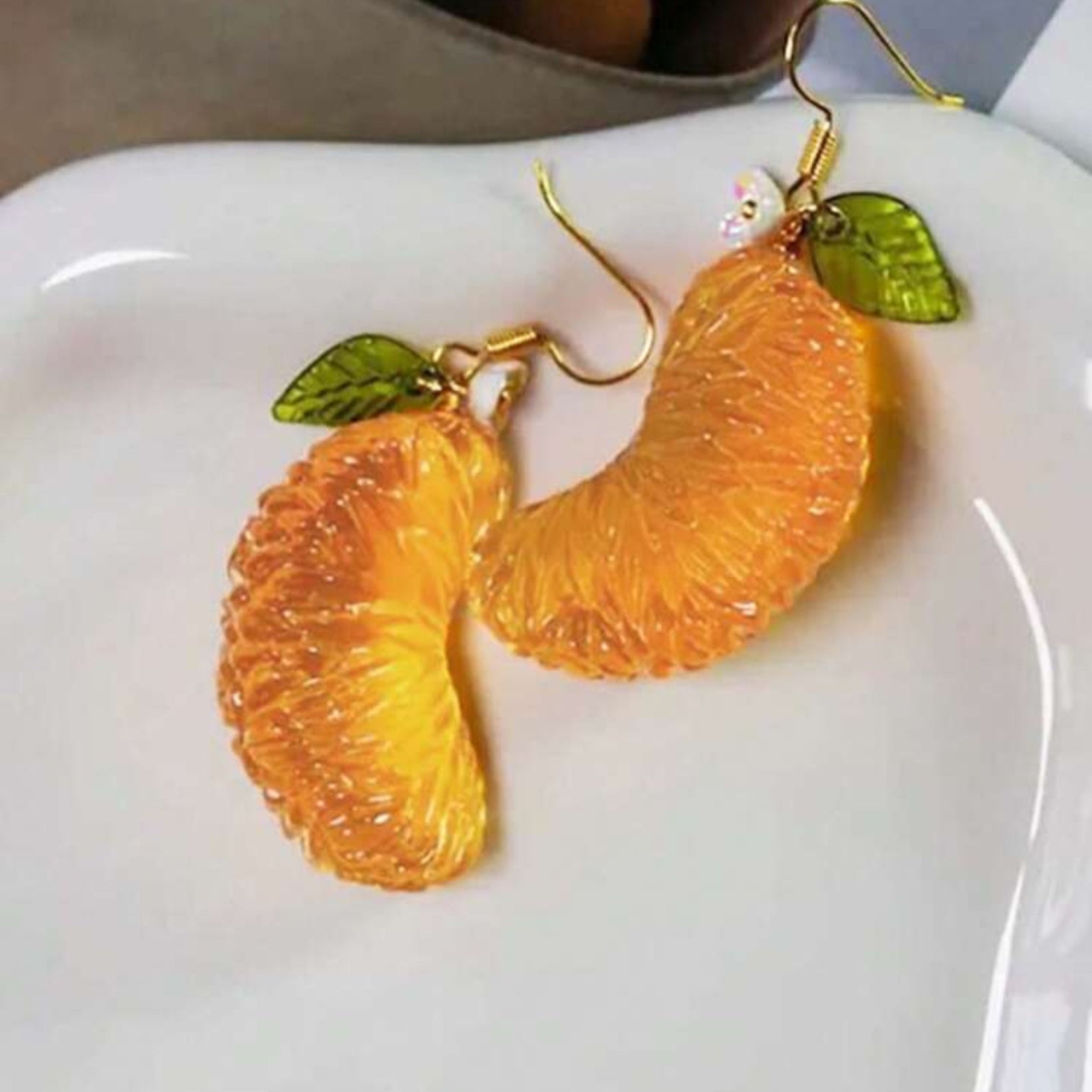 Orange slice earrings with green leaves on a white plate